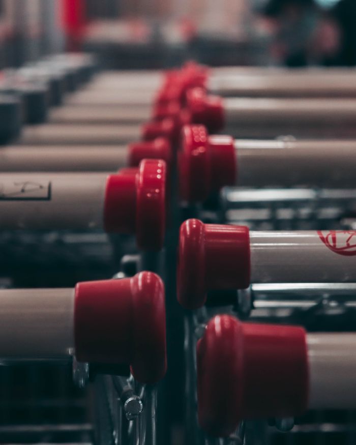 Close-up of supermarket shopping carts with red handles aligned indoors.